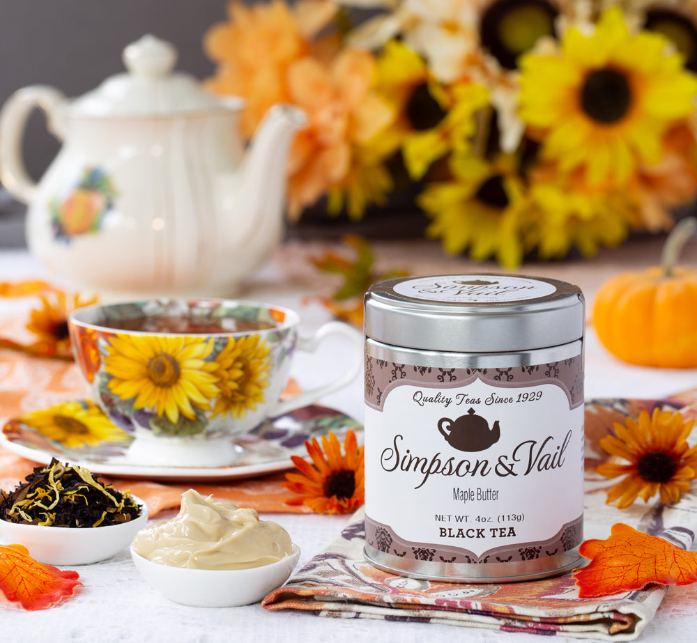 Tea canister with a teacup and tea leaves on a decorative table with flowers and pumpkins.